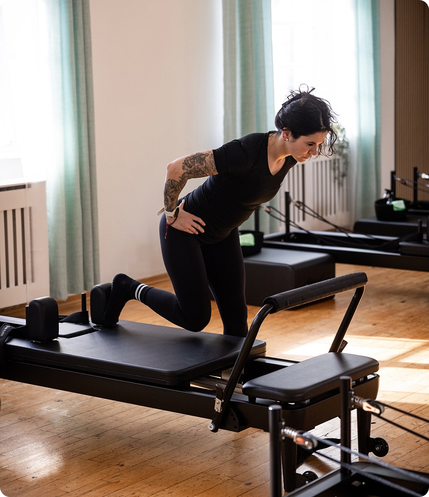 Reformer Pilates Trainerin auf einem Reformer Gerät.